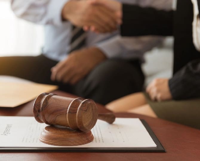 A close-up of a gavel on a document, with two people in the background shaking hands.