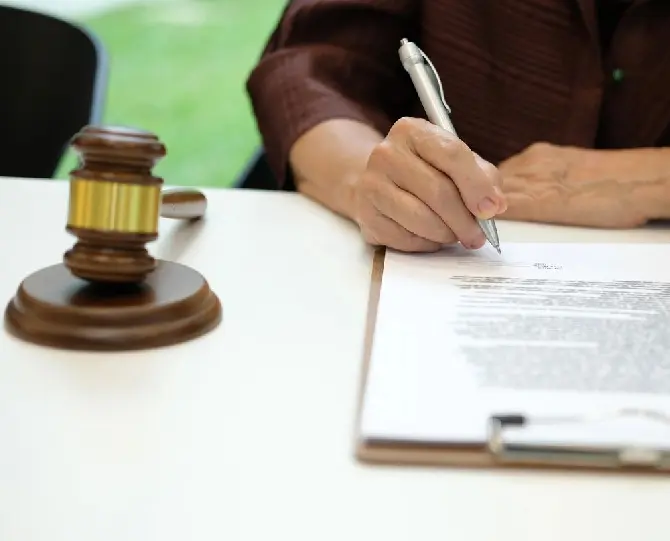 A person signing a document on a clipboard next to a wooden gavel.