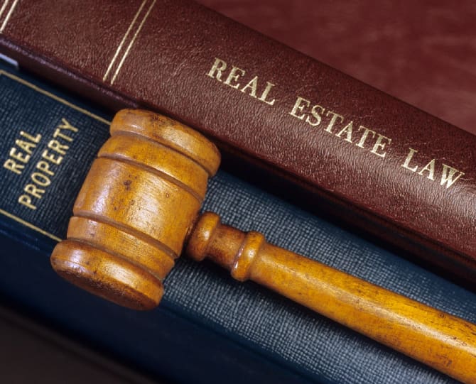 A wooden gavel rests on top of two books titled "Real Estate Law" and "Real Property.